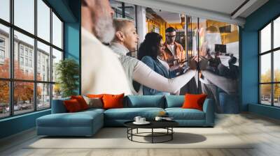 Multiethnic businesspeople attaching documents to glass wall in workshop Wall mural