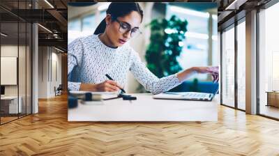 Pensive business woman noting idea for startup planning from web page on laptop computer,professional administrative manager making accountings of income using app on netbook in office interior Wall mural