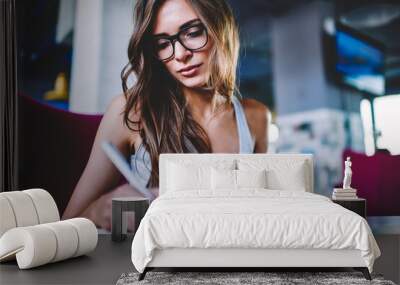 Pensive hipster girl in eyewear noting information from website browsed on smartphone Wall mural