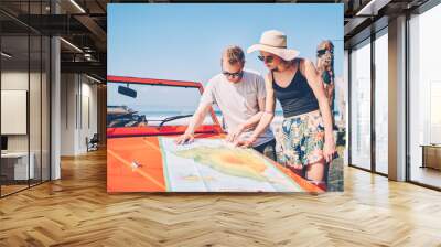 Pensive young male and female travelers reading map on convertible orange car choosing route for explore tropical island,romantic couple in love spending honeymoon in summer travel by automobile Wall mural