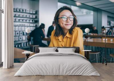 Portrait of cheerful hipster girl in optical spectacles for provide eyes protection looking at camera and smiling during blogging time in university classroom, concept of browsing and networking Wall mural