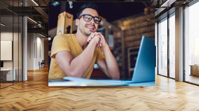 Portrait of cheerful male it professional working remotely with modern laptop device sitting at table and smiling at camera during break, happy man programmer in eyewear for vision correction Wall mural