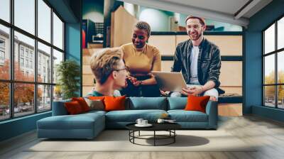 Positive male and female multiracial colleagues satisfied with cooperation share ideas and opinions,  cheerful creative guy with laptop computer talking with friend on meeting planning startup Wall mural