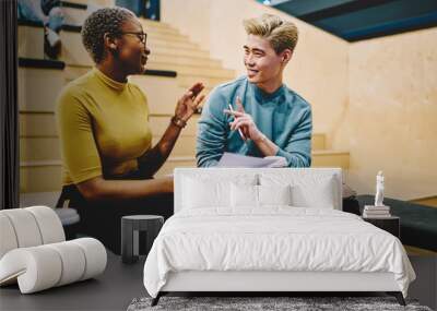 Positive multiracial colleagues gesture while discussing ideas and opinions about common project, smiling hipster male and female friends having communication on free time in college campus Wall mural