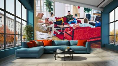 Positive young male and female persons spending free time together in comfortable stylish interior of modern frat, diversity crew of colleagues sitting in lounge zone on free time in coworking office. Wall mural