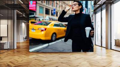 Serious woman in elegant formal wear waiting for taxi cab near traffic on road hurry up for important business meeting with company partners, attractive female trader with takeaway cup outdoors Wall mural