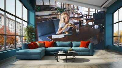 Smiling woman sitting with burger in cafe Wall mural