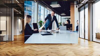 Successful male boss dressed in formal wear communicating with employees during brainstorming meeting for checking data information from financial report, group collaborating in office interior Wall mural