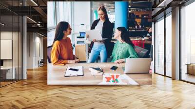 Successful three female designers collaborating on developing own fashion company in stylish studio.Young women using internet connection and modern laptop computers for creating design collection Wall mural