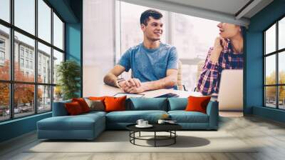 Two successful smiling teenagers casual dressed sitting desktop with netbooks connected to wifi, happy hipster guy looking at cheerful girl at coworking space, concept of technology and communication Wall mural