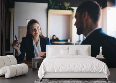 Young female employee listening to team leader explaining new strategy in office Wall mural