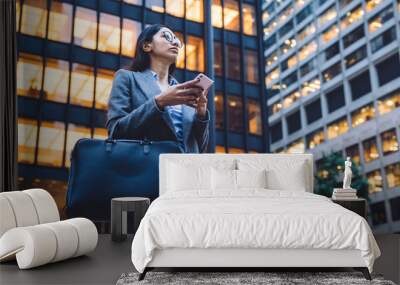 Young female with smartphone standing by skyscraper Wall mural