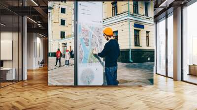 Young male traveler using modern smart board with map and useful information for tourists, caucasian hipster guy searching train on electronic device on street with wifi connection and touchscreen . Wall mural