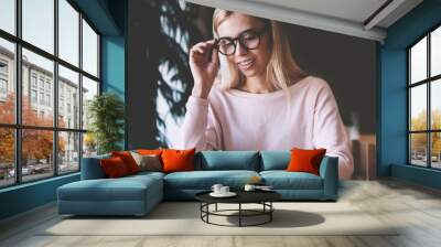 Young prosperous hipster girl in spectacles reading positive news about university student's life in campus, successful female blogger happy to read good email from follower in social network Wall mural