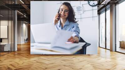 Young woman laughing while talking on cellphone in office Wall mural