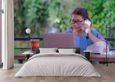 A middle-aged woman is talking on the phone while looking at her laptop Wall mural