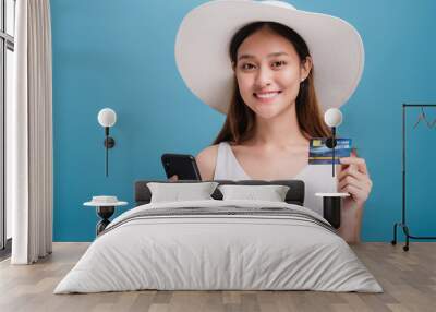 Asian smiling beautiful women wear a wide hat and sunglasses using smartphone shopping online with credit card isolated in blue color background.Concept of Travel business with Promotion and Sale. Wall mural