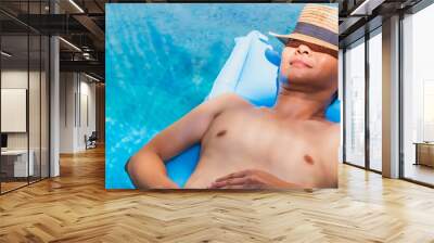 Asian traveler man sleep on pool float air mat in the swimming pool in tropical resort hotel background.Concept of a happy summer holiday travel. Wall mural