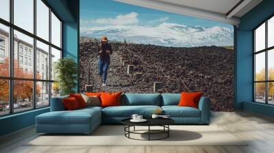 Asian woman travelers walk on the ground caused by volcanic ash with snow mountian background.Hiking and adventure travel concept. Wall mural