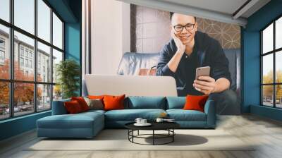 Happy asian businessman using smartphone while sitting on sofa at home office background.Concept of young people working mobile devices. Wall mural