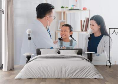 Professional doctor wearing white coat using stethoscope to examine kid patient with her mother in hospital background.Concept of disease treatment and health care in hospitals. Wall mural