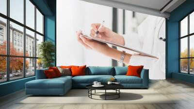 The female doctor is holding and writing medical report on hand to treat the patient in hospital.The concept of good health care by regularly checking health. Wall mural