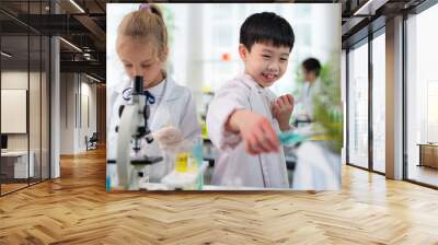 Asia cute boy wearing lab coat pouring blue solution from test tube into the plant pot in the elementary classroom. Learning chemistry and do the experiment in the school Wall mural