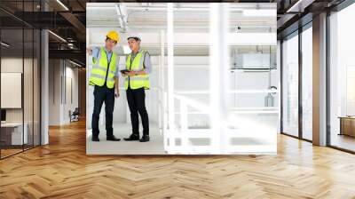 Senior and junior engineers discussing on work in the office plant. Junior hold paper roll and point to equipment and explain to senior engineer with copy space. Engineering and design concept. Wall mural