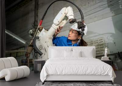 Technician woman check the robotic arm machine in the factory. Worker wearing safety helmet, glasses and uniform. Preventive maintenance to prevent breakdown. Service and repair concept Wall mural