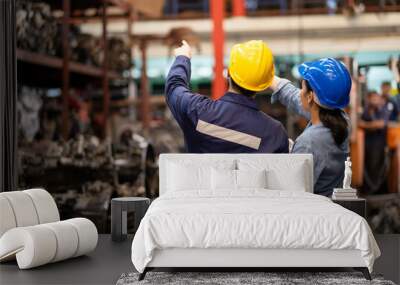 Two engineer or manager worker wearing safety helmet standing in the automotive part warehouse. Man and woman point forward to spare part in the rack. Inspector and quality check concept. Wall mural