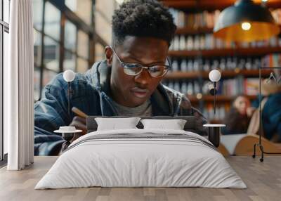 Focused millennial african american student in glasses making notes writing down information from book in cafe preparing for test or exam, young serious black man studying or working in coffee house Wall mural