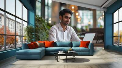 indian businessman working on laptop in modern office lobby space. Young indian student using computer remote studying, watching online webinar, zoom virtual training on video call meeting. Wall mural