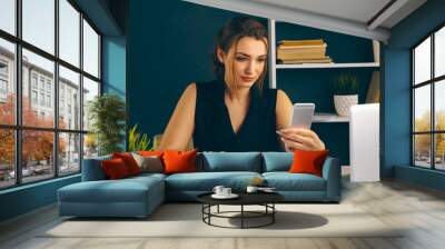 Attractive female person using phone in office sitting at the desk isolated Wall mural