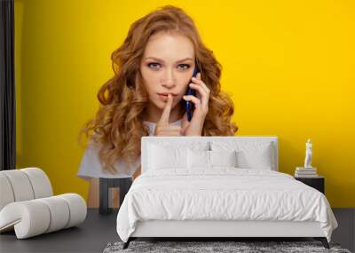 Blond curly hair woman posing with silence getsure holding phone Wall mural