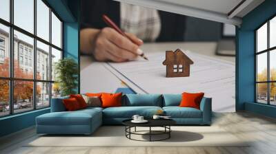 Close up wooden toy house with Woman signs a purchase contract or mortgage for a home, Real estate concept. Wall mural