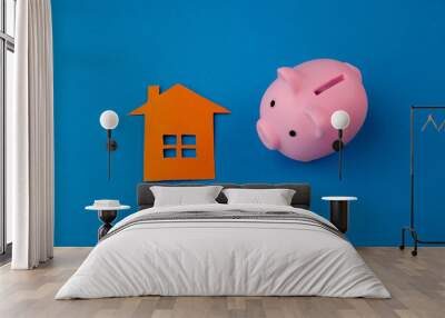 Mortgage concept. Little paper house next to a piggy bank on blue background Wall mural