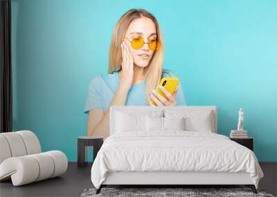 Young woman over in sunglasses over isolated blue background surprised and sending a message. Wall mural