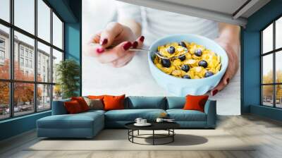 A woman is eating yogurt with cereal and berries for breakfast, holding a spoon, close-up hands, a healthy diet and a diet concept, summer berries Wall mural