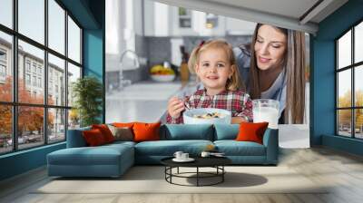 Smiling little girl enjoying breakfast with her mother Wall mural