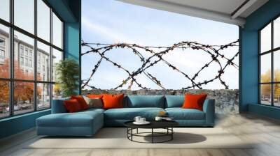 loops of barbed wire on an old concrete fence, against a blue sky Wall mural