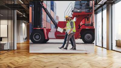 Cheerful Caucasian engineer wearing safety vest standing by shipping container terminal talking discussing information to African collaborator. Transportation business. Logistic industrial concept Wall mural