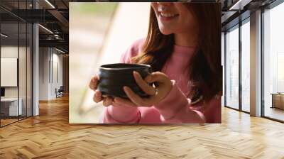 Portrait of Beautiful young Asian woman drinking fresh tea in a vintage ceramic cup bowl sitting by the balcony. Morning summer light feeling warm and relax. Healthcare or Herbal medicine concept. Wall mural