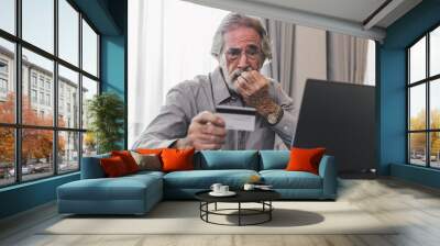 Upset senior elderly man holding credit card by laptop having trouble worry finance safety data or online payment security. Bank client concerned about problem with credit card, financial fraud threat Wall mural