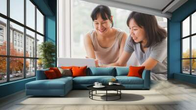 Young cheerful happy Asian university student working on laptop notebook together at coffee cafe. Attractive lesbian couple as a content creator talking sharing idea with relax moment. Wall mural