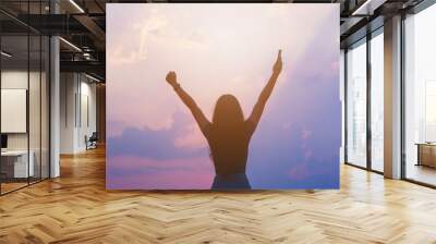 Young empowered lady raising her hands up to the sky, hand holding smart phone against sunset sky Wall mural