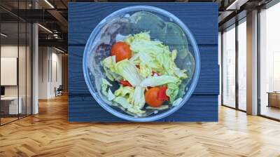 food from fresh green salad and red tomatoes in a plastic plate stands on a black wooden table Wall mural