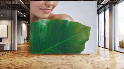 Close-up of a woman with glowing skin, holding a large green leaf covered in dew droplets. Perfect for promoting natural beauty, eco-friendly skincare, and wellness products that emphasize purity and Wall mural