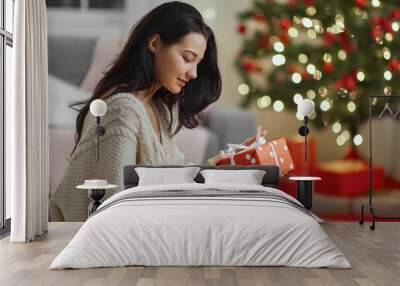 Curious happy romantic woman standing against Christmas tree background. Close-up portrait of smiling lady ready to open of the present after in the wrapped gift box Wall mural