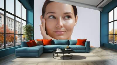 Happy beautiful young adult woman touching her perfect face with healthy shiny skin, hand on chin. Beauty photo of gorgeous girl after morning beauty cosmetic routine finishes daily makeup on gray Wall mural