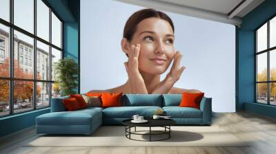 Skincare. Woman with beautiful face touching healthy facial skin. Beautiful portrait of smiling Asian girl model with natural makeup enjoys glowing hydrated skin on blue background closeup. High Wall mural